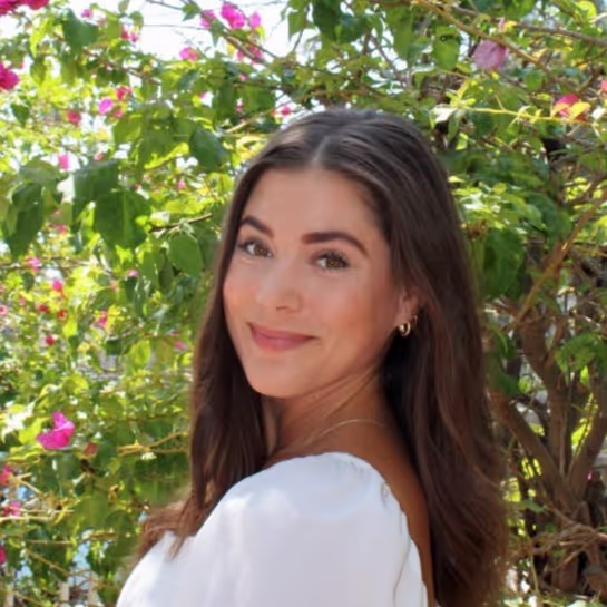Woman smiling in white top amid flowering green bush with pink blossoms